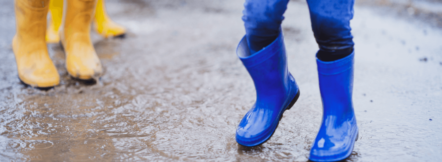 Child's legs in blue wellington boots playing with a puddle outdoors on a rainy day